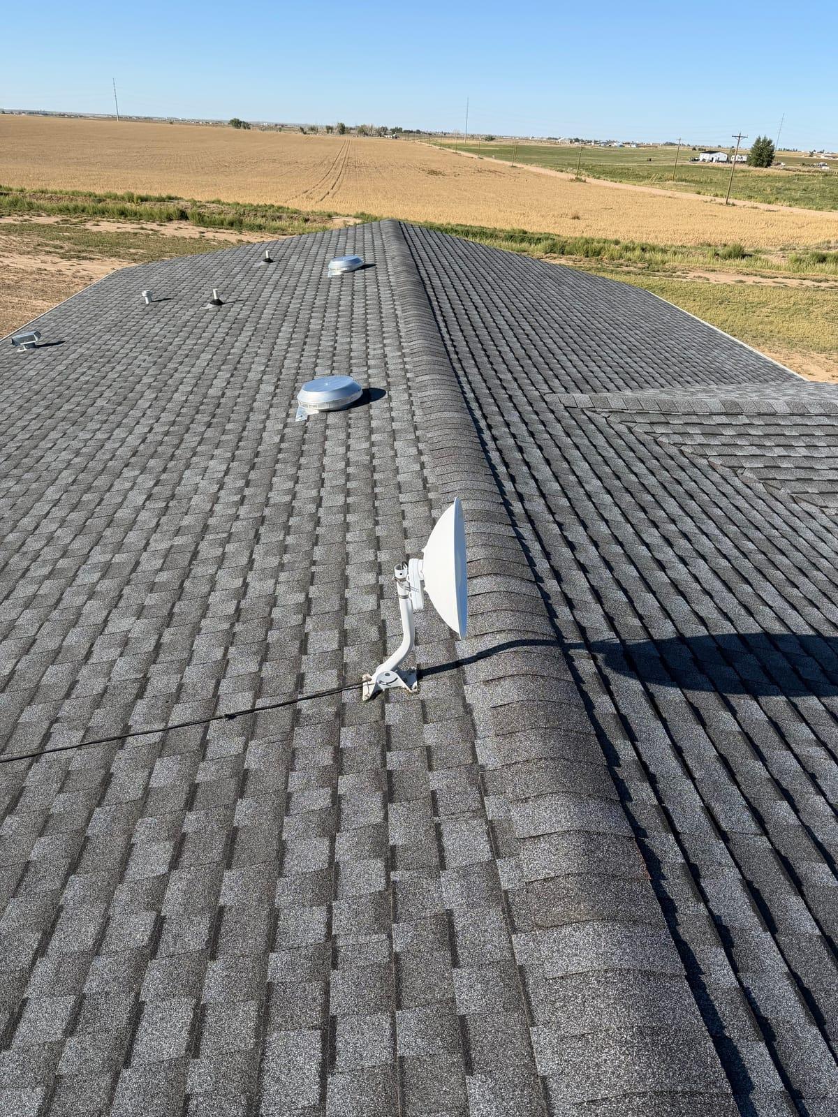 Grey architectural shingle hip roof on a rural Colorado property, with open farmland stretching to the horizon