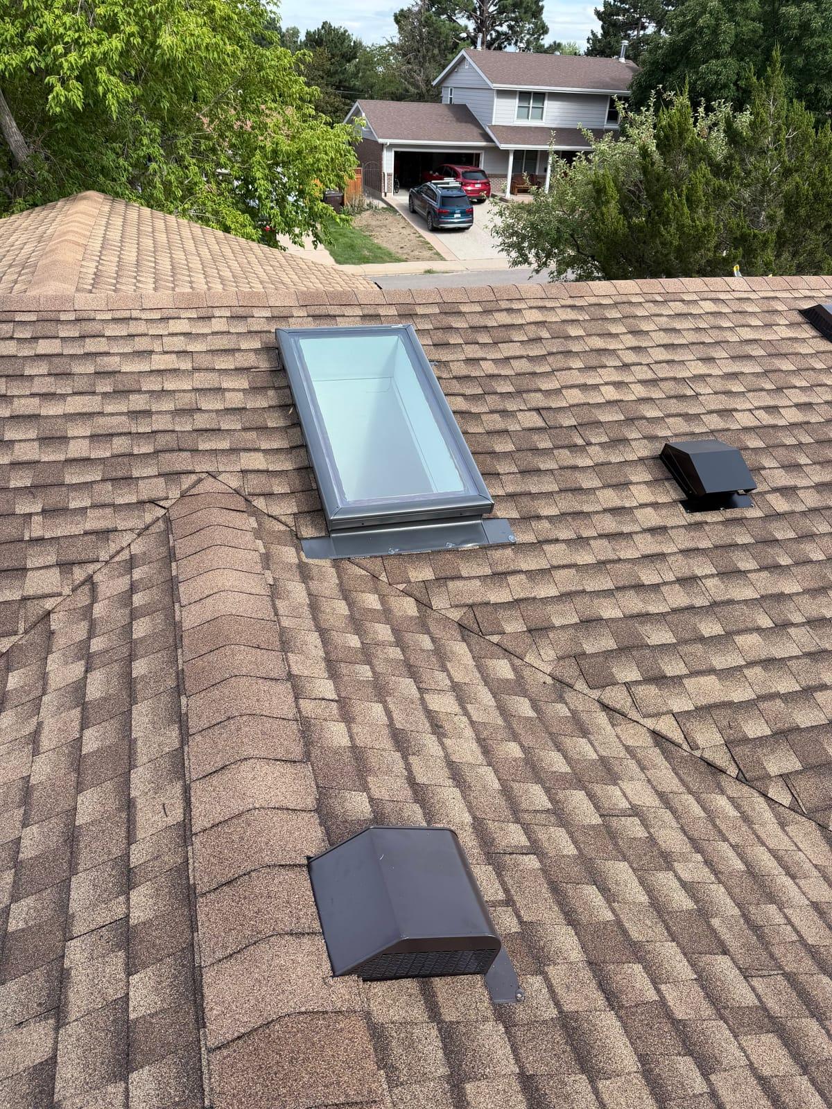 Weathered-wood brown architectural shingles around a newly flashed skylight, with two box vents nearby